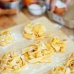 Homemade raw noodles sprinkled with flour on wooden chopping board on kitchen table