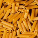 Detailed shot of uncooked penne pasta with distinct texture, ideal for food backgrounds.