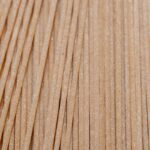 Vertical close-up of uncooked whole wheat pasta strands on a surface.